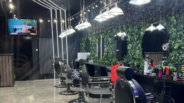 The shop floor: a row of barber chairs under pendant lights, a green plant wall behind